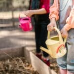 Dwoje dzieci podlewa rośliny w ogrodzie agroturystycznym