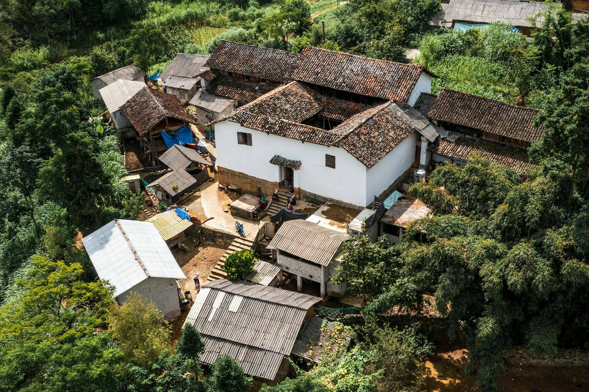 Wiejska osada z tradycyjnymi domami otoczona zielonymi polami i lasem