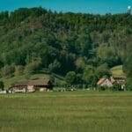 Gospodarstwo agroturystyczne przy lesie, zielone łąki i wzgórza pod błękitnym ni
