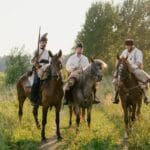 Jeźdźcy w historycznych mundurach jadą konno wiejską ścieżką